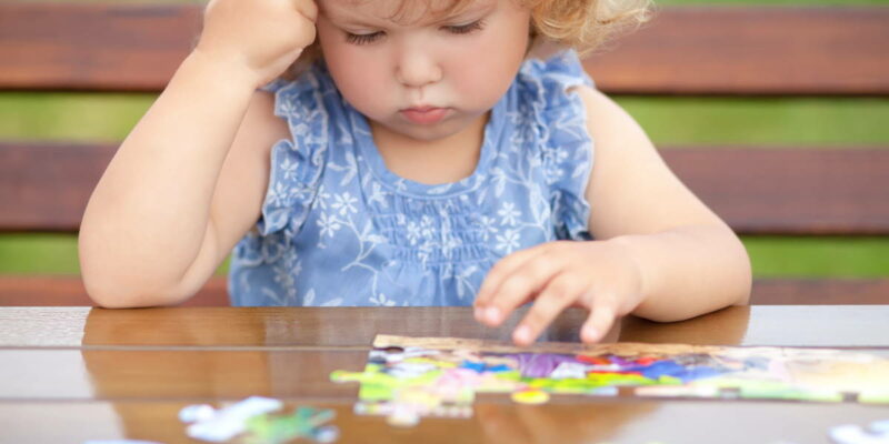 blonde unhappy toddler girl, solving puzzle on a table, hard difficult task. Early education and developement. Little genius concept. Emotional. (blonde unhappy toddler girl, solving puzzle on a table, hard difficult task. Early education and develope